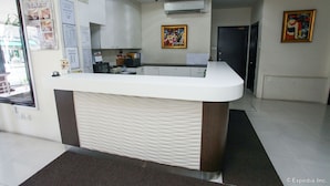 Una recepción con mostrador blanco y base marrón, un tablón de anuncios con varios avisos y un cuadro en la pared.