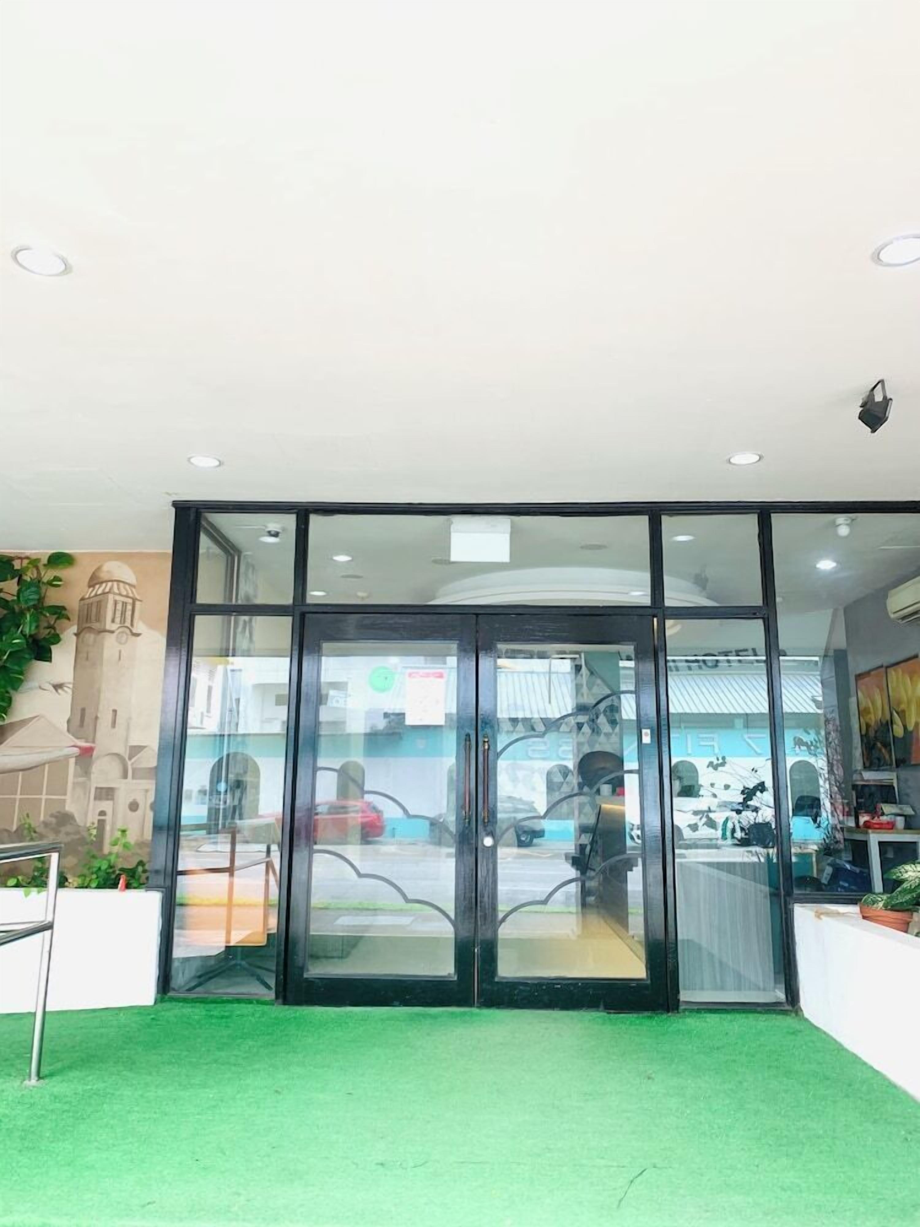 A hotel entrance with a glass door, a green carpeted area, and a mural of a building on the wall.