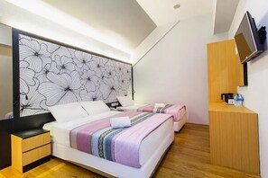 A modern hotel room with a large bed, a smaller bed, a wooden nightstand, a TV mounted on the wall, and a wooden desk with a chair.
