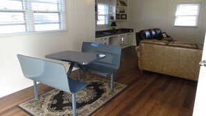 A living room with a brown leather sofa, a dining table with two chairs, a kitchen area with a stove, and a window with blinds. -  EZ - GO Lodging 3.7 mi Green Pond Landing(Lake Hartwell) Clemson Univ 15 mil. (Anderson)