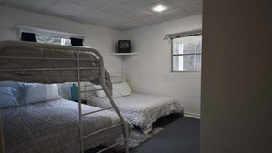 Une chambre de dortoir avec des lits superposés, une petite étagère sur laquelle se trouve un téléviseur, et une fenêtre.