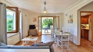 A spacious living room with a sofa, a TV, and a dining area with a table and chairs. There is a kitchen visible through an open doorway. - 2 198 / 5 000
Cozy cottage with private garden and terrace – peaceful setting (Le Bar-sur-Loup)