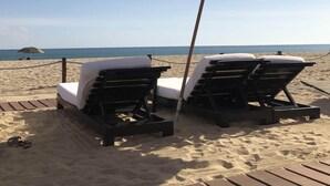 Two lounge chairs with white cushions and a large umbrella on a sandy beach with a clear view of the ocean. - 2 Bedroom Serenity Pool View (San José del Cabo)