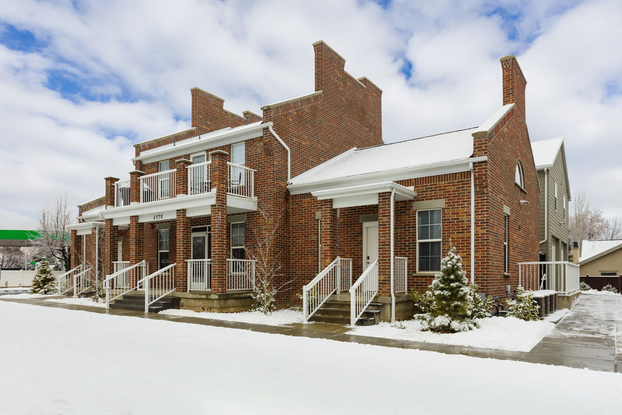 A two-story brick building with a balcony on the second floor, a covered front porch, and a snow-covered ground.