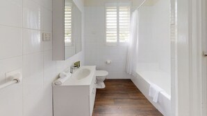 Un baño con azulejos blancos, un lavabo, inodoro y bañera.