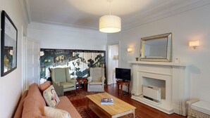 Una sala de estar con sofá, sillones, una mesa de centro, chimenea y un cuadro grande en la pared.