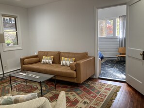 Een woonkamer met een bruine leren bank, twee gestreepte kussens, een glazen salontafel en een kleurrijk vloerkleed.