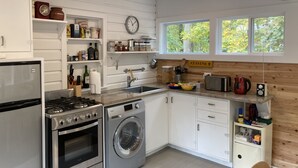 Una cocina funcional con armarios blancos, estufa, lavadora y ventana con vista a árboles.