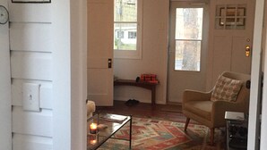 Un salón con un tapete estampado, un sillón, una mesa de centro y una puerta con un cartel de cerveza Red Stripe.