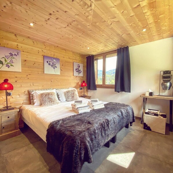 Un dormitorio con paneles de madera, una cama, dos lámparas de noche, un ventanal con cortinas y una mesita con una lámpara y una caja de pañuelos.