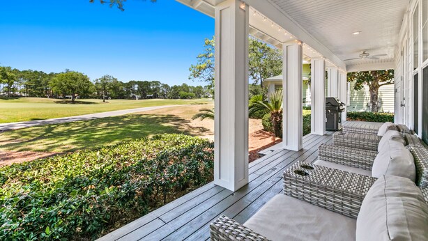 Un porche cubierto con muebles de mimbre y vistas a un campo de golf.
