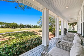 A covered porch with wicker furniture and a view of a golf course.