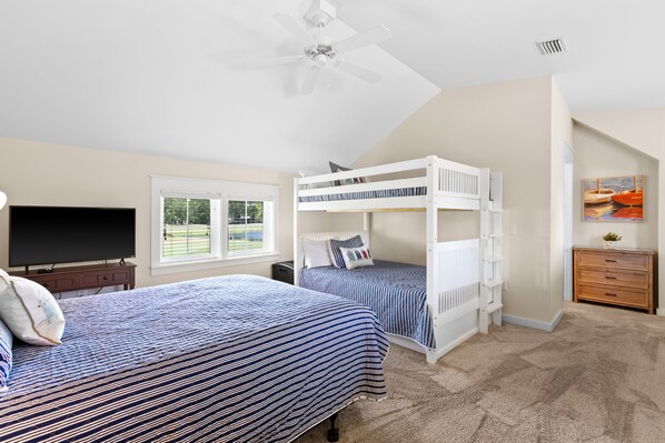 A bedroom with bunk beds, a television, a dresser, and a window with a view of a tennis court.