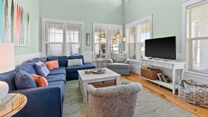 Una sala de estar con un sofá modular, un sillón gris, una mesa de centro y un televisor sobre un mueble blanco.