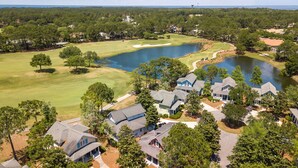 Vista aérea de un campo de golf con un estanque, rodeado de casas residenciales con techos inclinados.