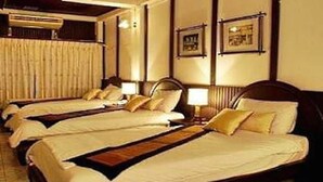 Ein Hotelzimmer mit vier Einzelbetten, jedes mit Kissen und Decke. Es gibt ein Holz-Kopfteil, einen Nachttisch mit Lampe sowie eine Wand-Klimaanlage.