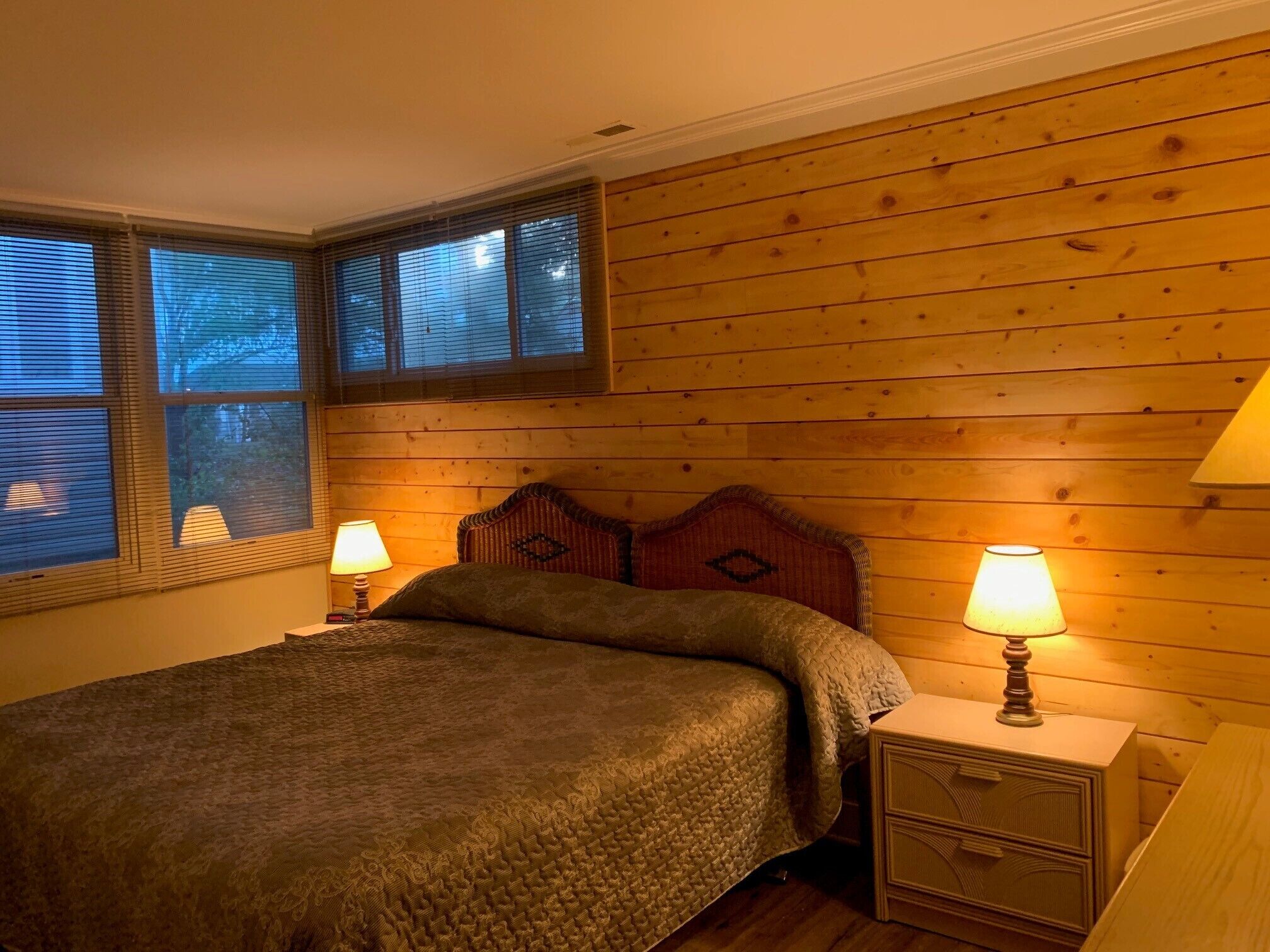 Un dormitorio con cabecera de madera, dos mesitas de noche con lámparas y una cama con manta texturizada.