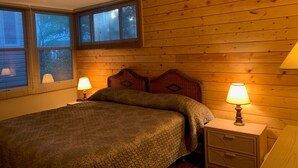 Een slaapkamer met een houten hoofdbord, twee nachtkastjes met lampen, en een bed met een gebreid plaid.