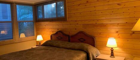 Un dormitorio con cabecera de madera, dos mesitas de noche con lámparas y una cama con manta texturizada.