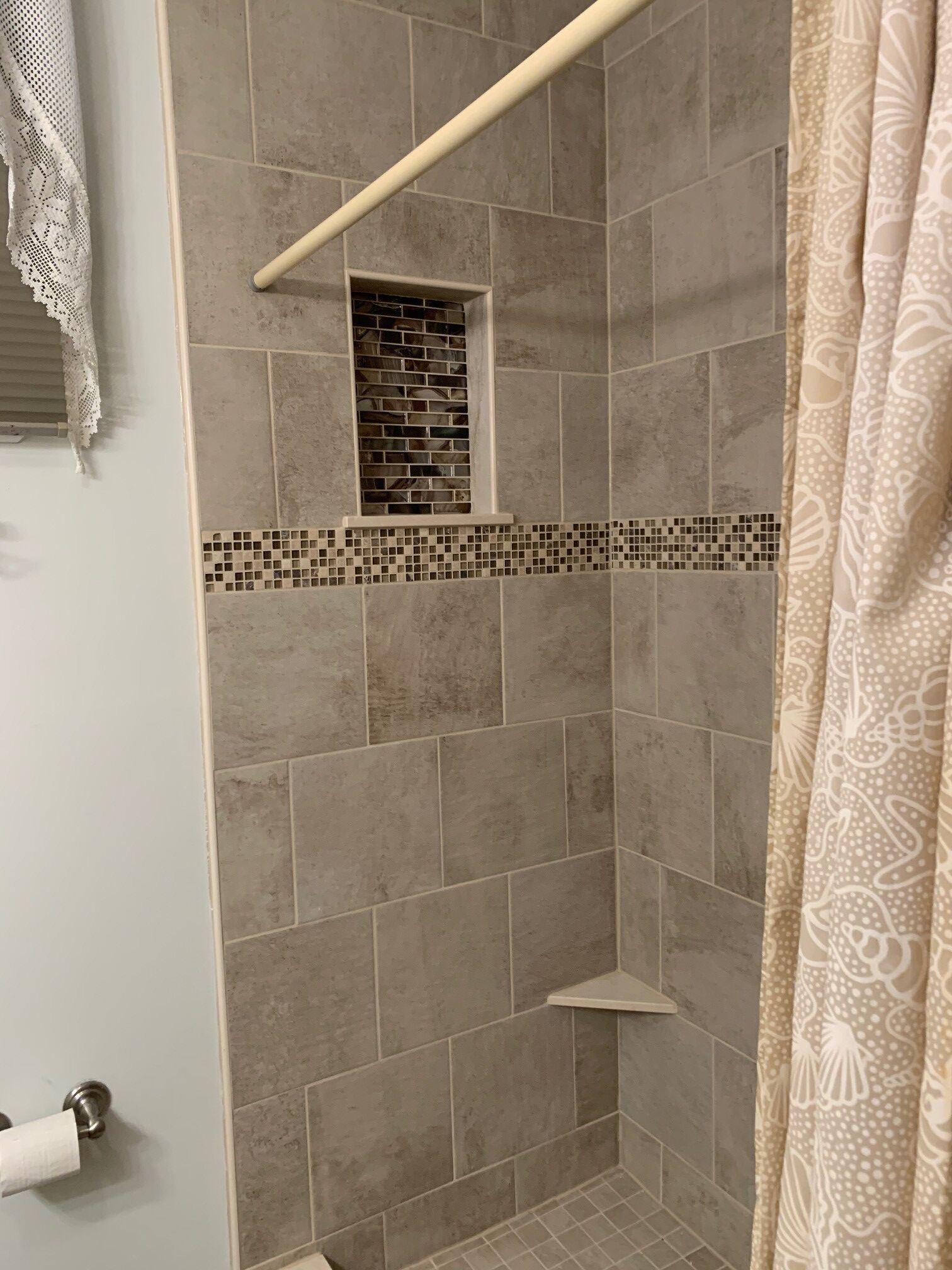A shower area with beige tiles, a small window, and a towel rack.