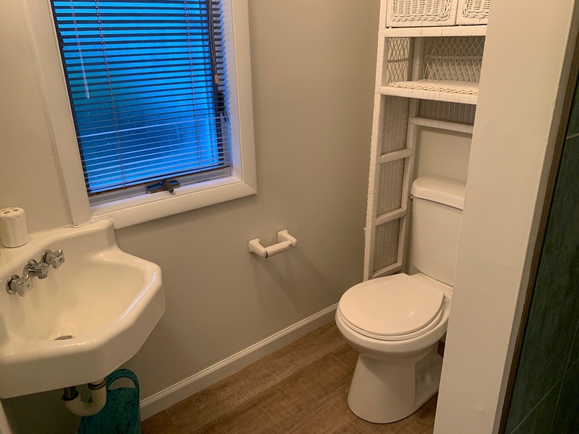 Un bagno con lavandino bianco, water e mensole in vimini.