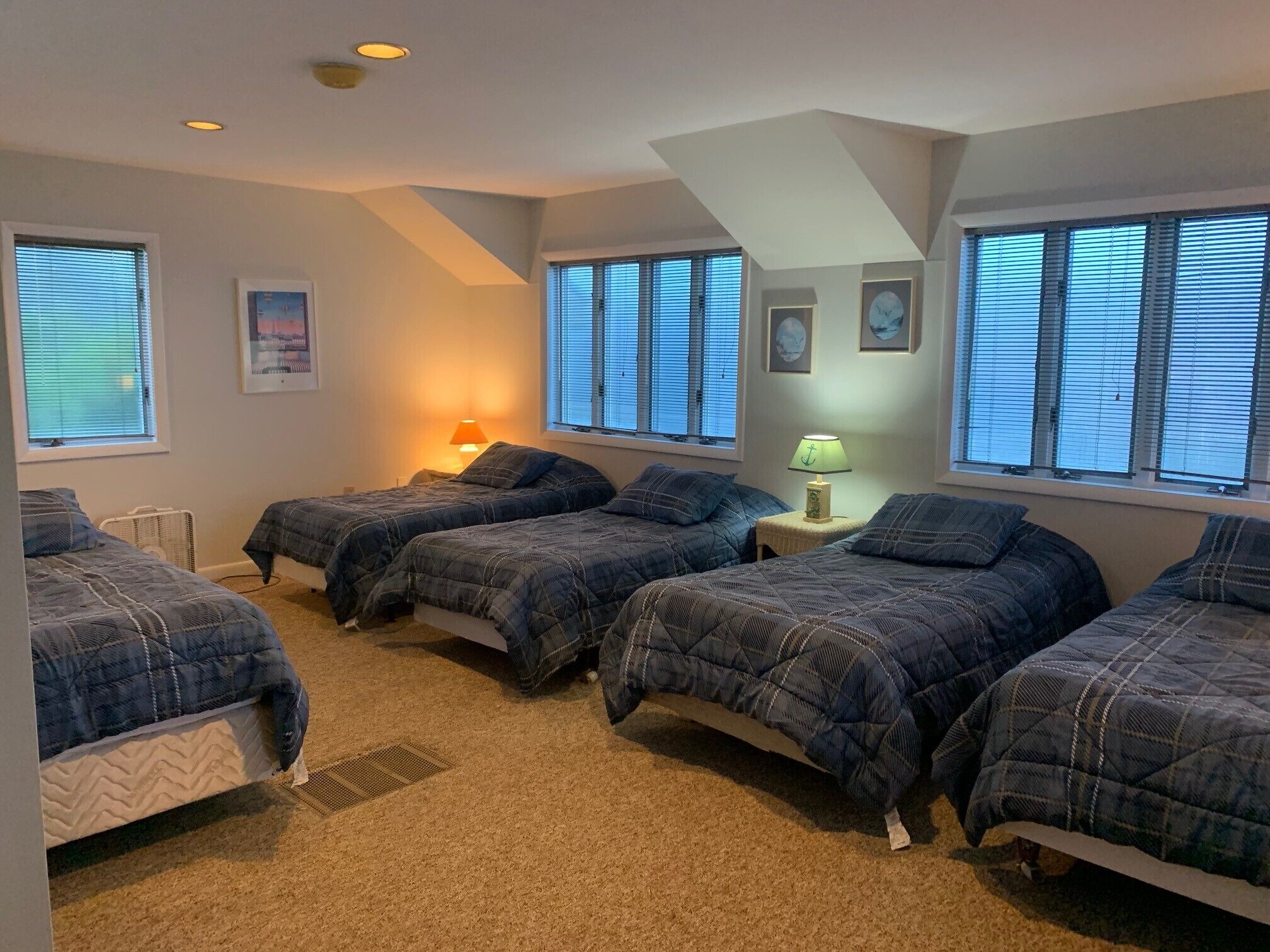 A bedroom with four beds, a ceiling fan, and a window with blinds.