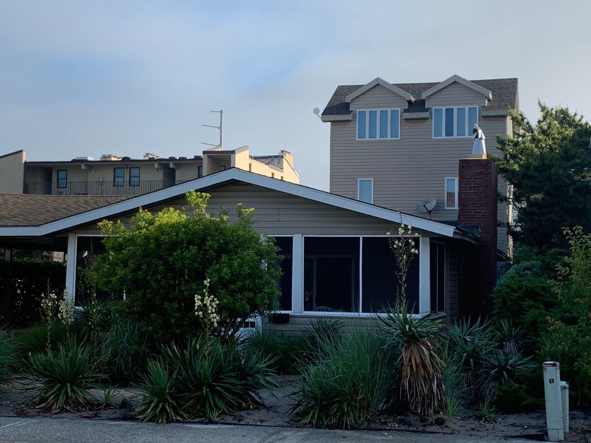 A two-story house with a covered porch, surrounded by various plants and shrubs.
