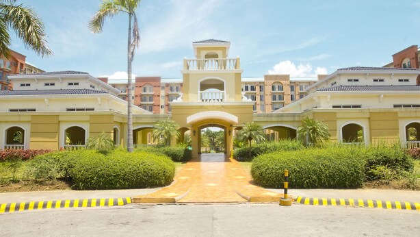 A hotel entrance with a central archway, surrounded by greenery and palm trees. - Chateau Elysee - Seine Cluster (Parañaque)