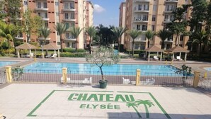 A swimming pool area with a sign reading "CHATEAU ELYSÉE" surrounded by palm trees and a multi-story building in the background. - Chateau Elysee - Seine Cluster (Parañaque)