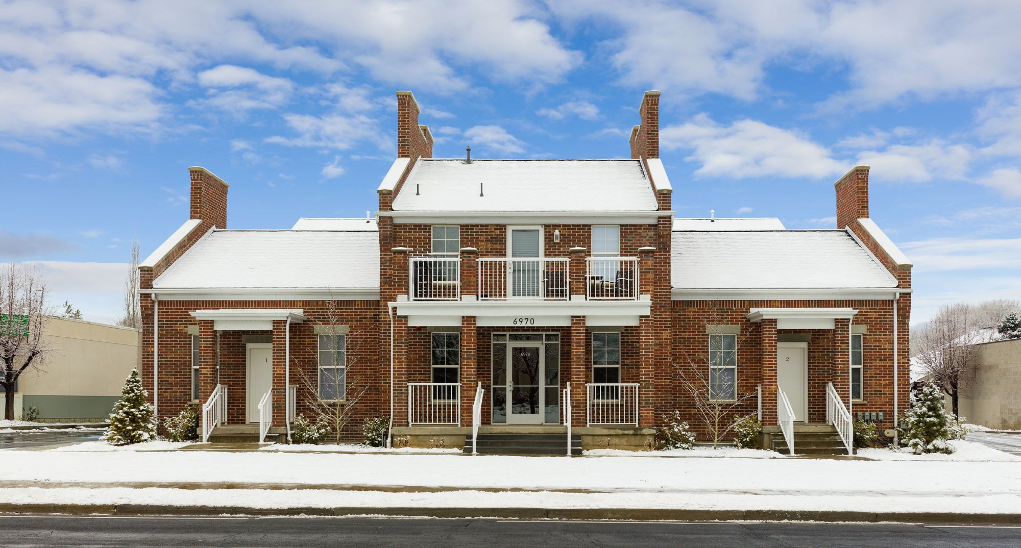 A two-story brick building with a symmetrical facade, a central entrance, and a snow-covered roof.
