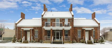 A two-story brick building with a symmetrical facade, a central entrance, and a snow-covered roof.