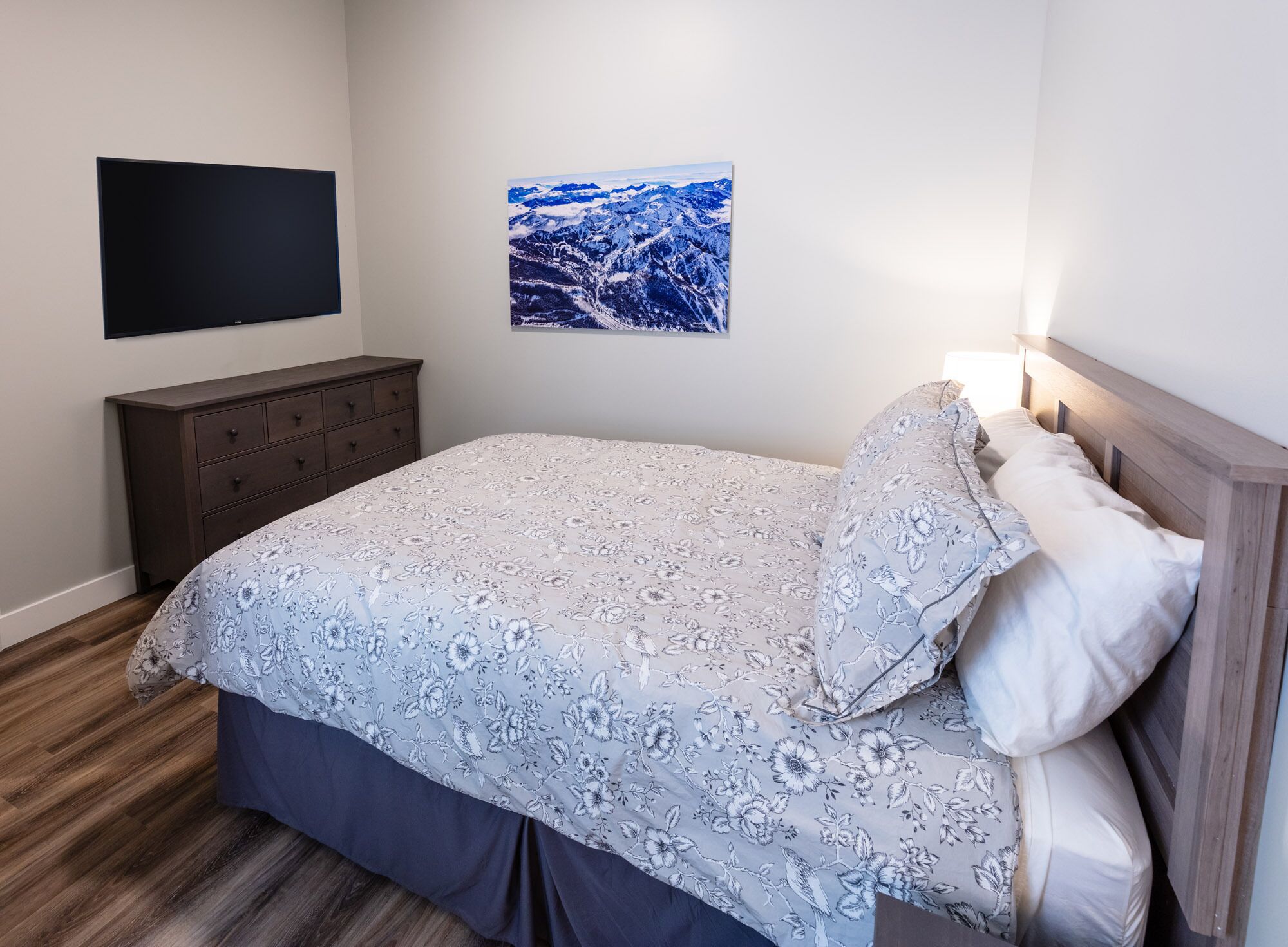 A bedroom with a bed, a dresser, a flat-screen TV, and a framed picture on the wall.