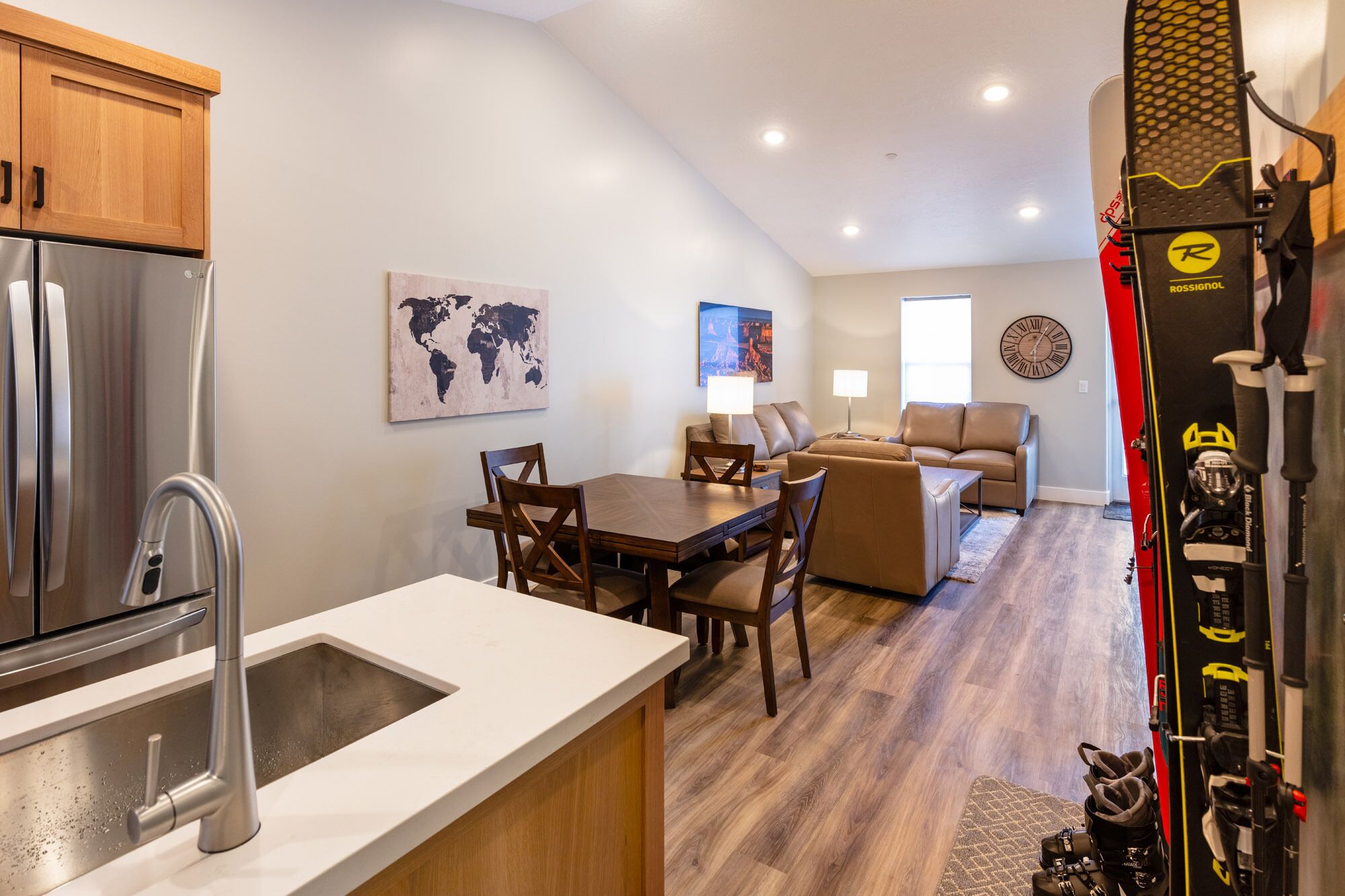 Una cocina moderna con un refrigerador de acero inoxidable, un lavamanos y un comedor con mesa y sillas. Cuenta con una sala de estar con un sofá y una lámpara.