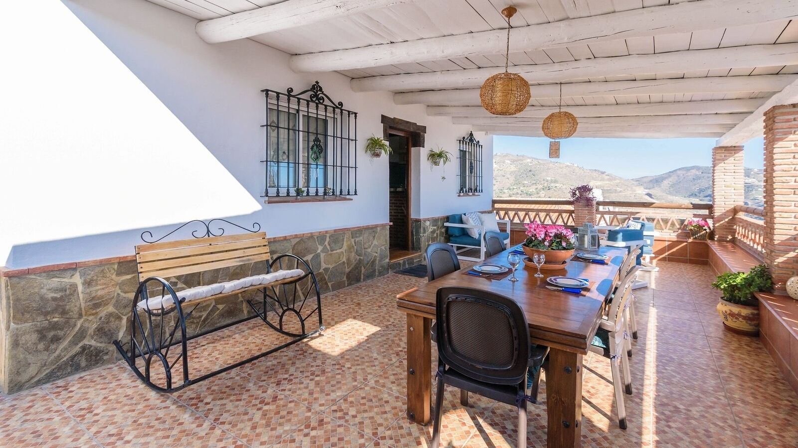 An outdoor patio with a wooden table and chairs, a bench, and a view of the mountains.