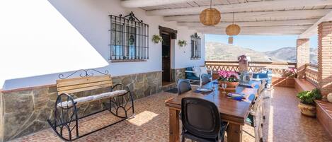 An outdoor patio with a wooden table and chairs, a bench, and a view of the mountains.