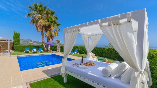 Zona privada de piscina amb un llit amb baldacín blanc, gandules i vista al mar.