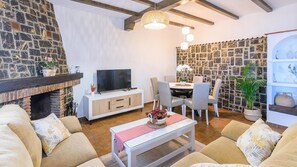 A living room with a stone wall, a fireplace, a TV, a dining area with chairs, and a sofa. - Villa Elvira Torrox by Ruralidays (Málaga)