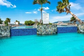 A pool area with clear blue water, stone walls, and a lifeguard sign. - Amazing Views & Beach Access w GENERATOR & Dishwasher. Check August discounts! (Saint Thomas)