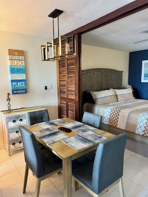 A room with a bed, a dining table with chairs, a wall-mounted light fixture, and a decorative sign. - Amazing Views & Beach Access w GENERATOR & Dishwasher. Check August discounts! (Saint Thomas)