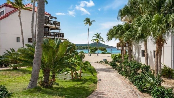 Un sendero que lleva a una playa con palmeras y un edificio con balcones.