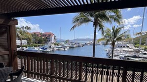 Un balcón con vista a un puerto deportivo, que incluye barcos y palmeras.