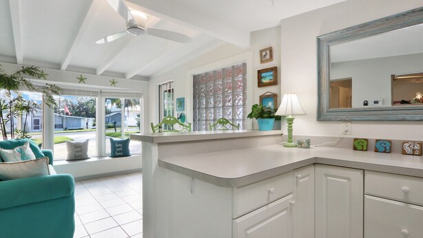 A bright kitchen with white cabinets, a large mirror, and a ceiling fan. - Old Florida Key West Cottage w/ river access (Jensen Beach)