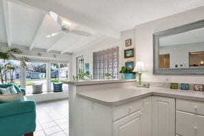 Une cuisine lumineuse avec des meubles blancs, un grand miroir et un ventilateur de plafond.