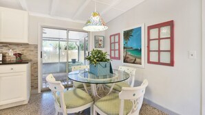 A dining area with a glass table, white chairs, and a hanging light fixture. - Old Florida Key West Cottage w/ river access (Jensen Beach)