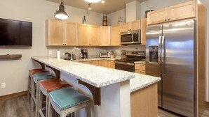 A modern kitchen with wooden cabinets, stainless steel appliances, and a granite countertop. - Beautiful 3-bed/2-bath Condo Looking Into Glacier National Park! (Columbia Falls)