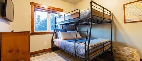 A bunk bed room with a window, a map on the wall, and a small wooden desk.