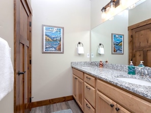 A bathroom with a granite countertop, wooden cabinets, a large mirror, and two framed pictures on the wall.