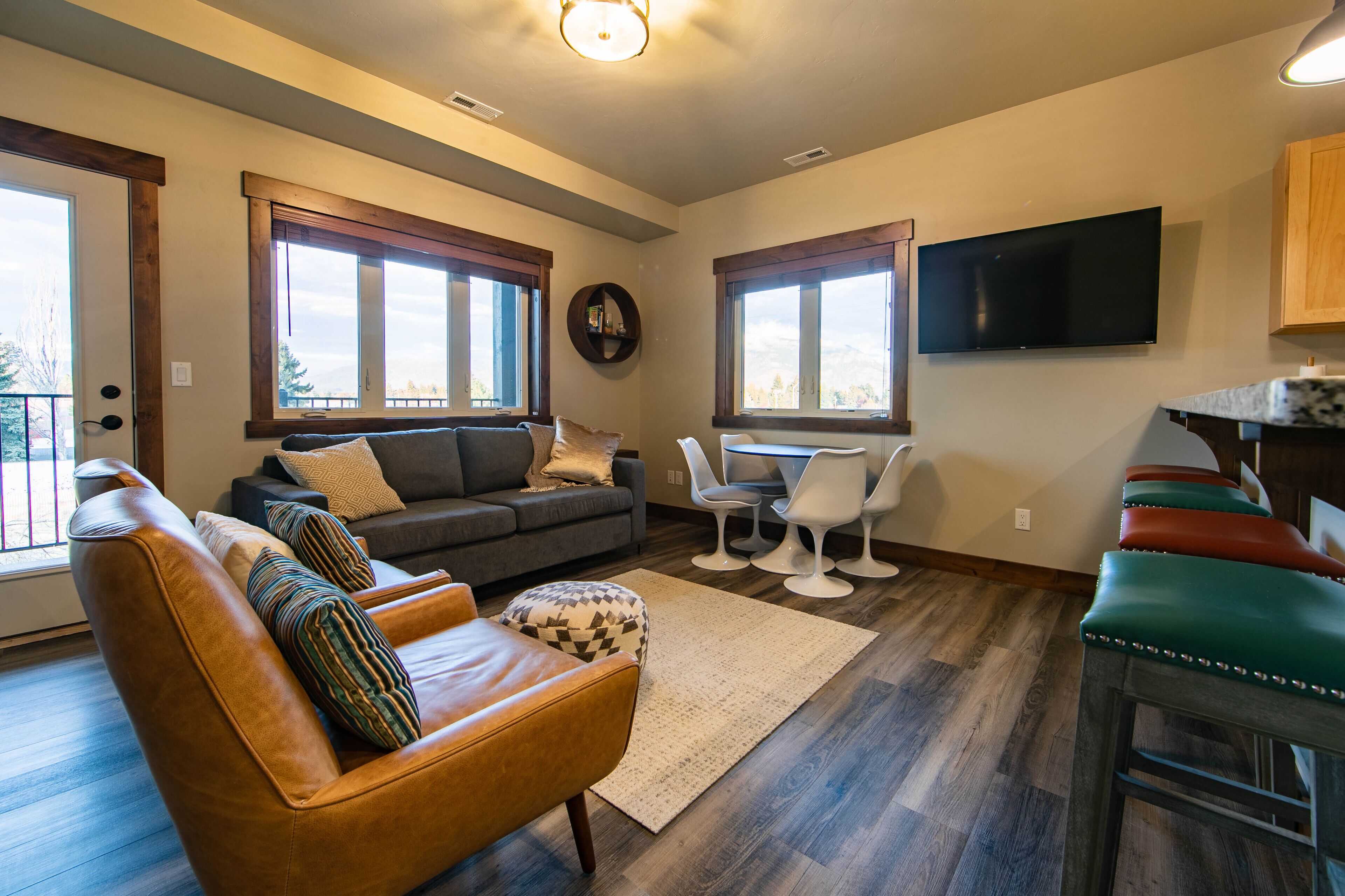 A living room with a sofa, armchair, and ottoman, a dining area with a table and chairs, and a TV mounted on the wall.