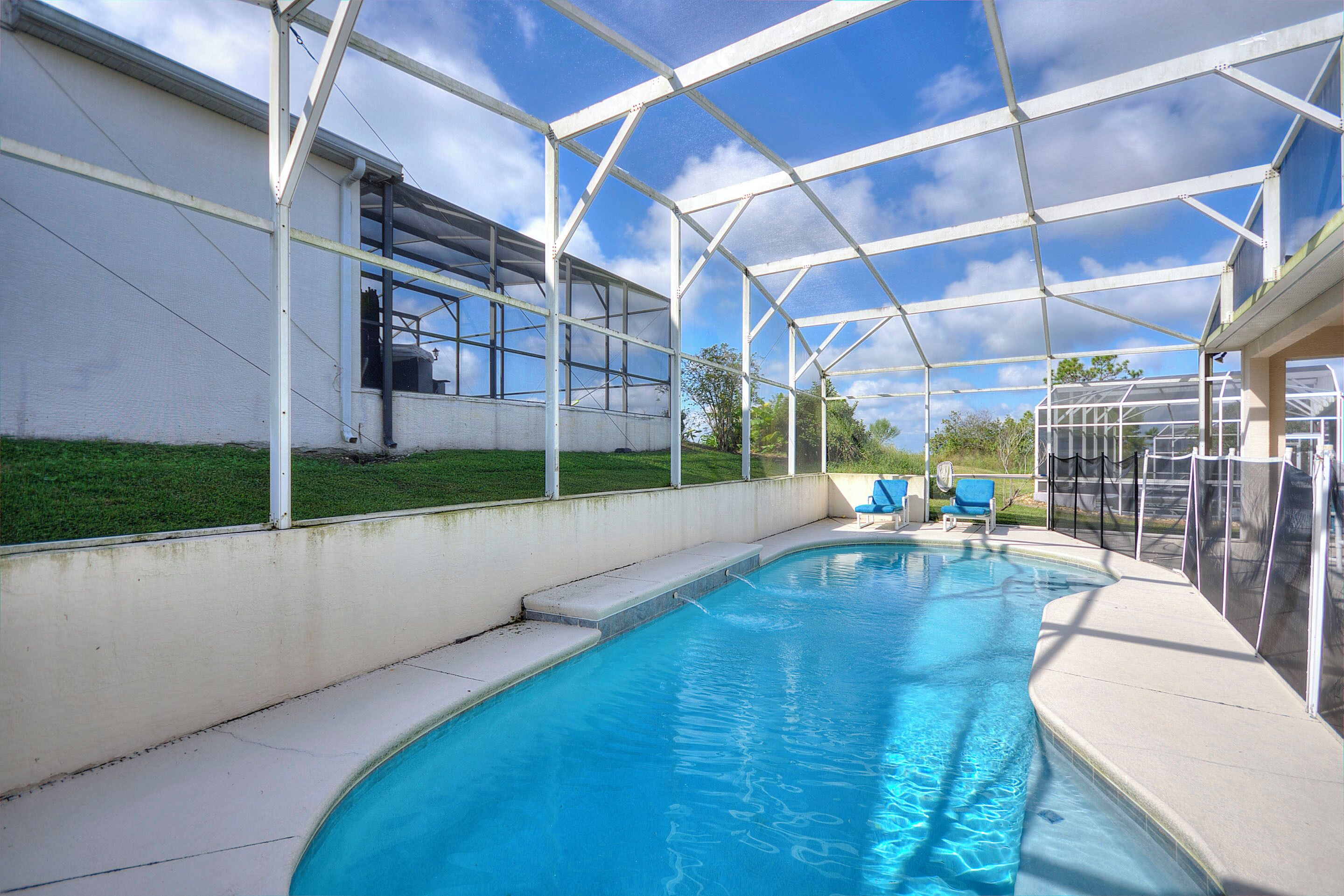 A swimming pool with a covered area, a white building, and a grassy area.