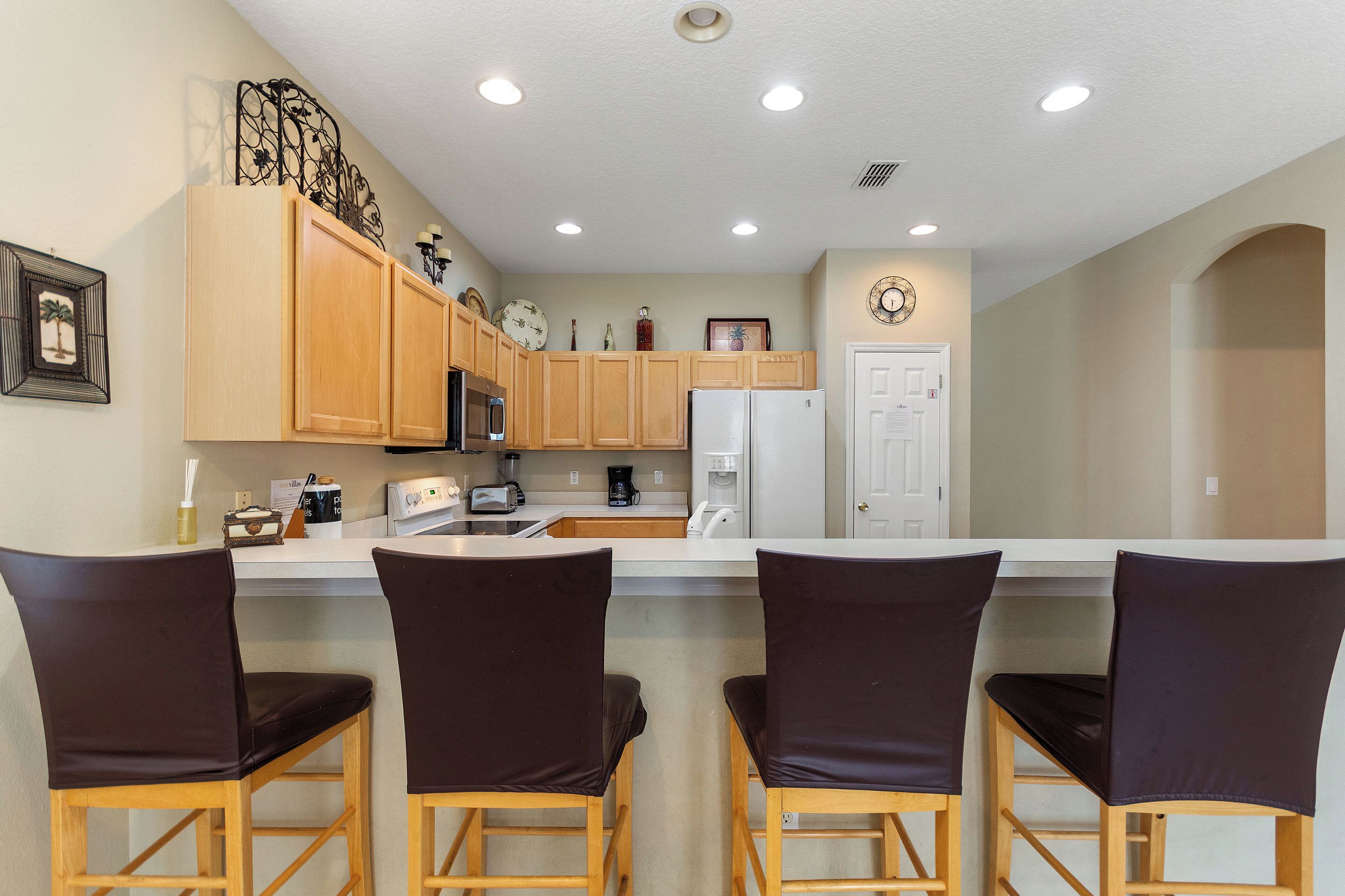 A kitchen with wooden cabinets, a white refrigerator, a coffee maker, and three bar stools.